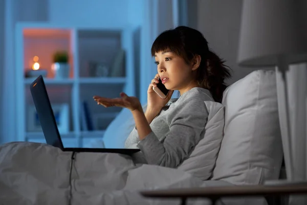 Mulher com laptop chamando no telefone na cama à noite — Fotografia de Stock