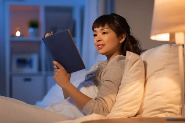 Молодая азиатка читает книгу в постели дома — стоковое фото