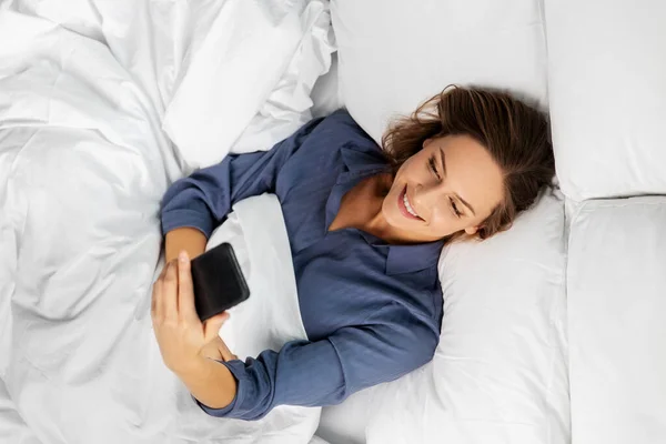 Mujer joven con smartphone acostado en la cama —  Fotos de Stock