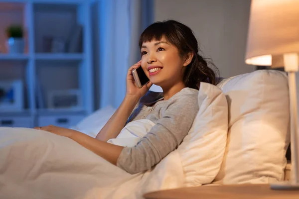 Asiático mujer llamando en smartphone en cama en la noche —  Fotos de Stock