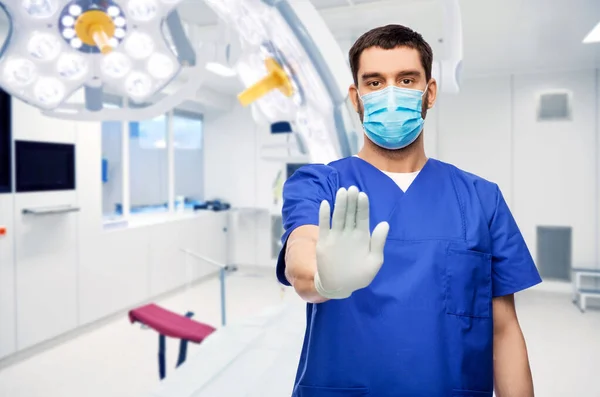 Чоловічий лікар у блакитній формі та маска, що показує зупинку — стокове фото