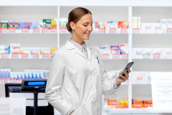 Felice medico femminile con smartphone in farmacia — Foto Stock