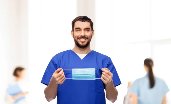 Médico varón sonriente en uniforme azul con máscara — Foto de Stock