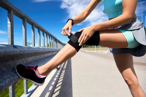 Mujer joven en banda de rodilla haciendo deportes al aire libre — Foto de Stock