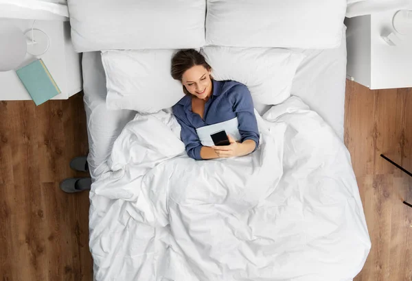 Mujer joven con smartphone acostado en la cama — Foto de Stock