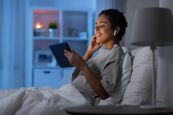 Frau mit Tablet-PC im Kopfhörer nachts im Bett — Stockfoto