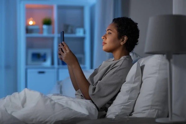 Afrikanerin mit Smartphone nachts im Bett — Stockfoto