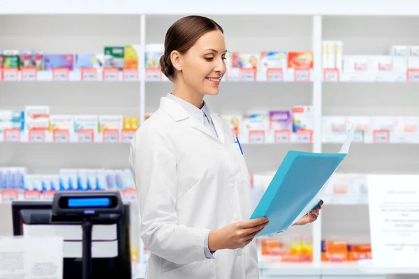 Sonriente médico femenino con carpeta en la farmacia — Foto de Stock