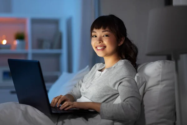 Mulher com laptop na cama em casa à noite — Fotografia de Stock