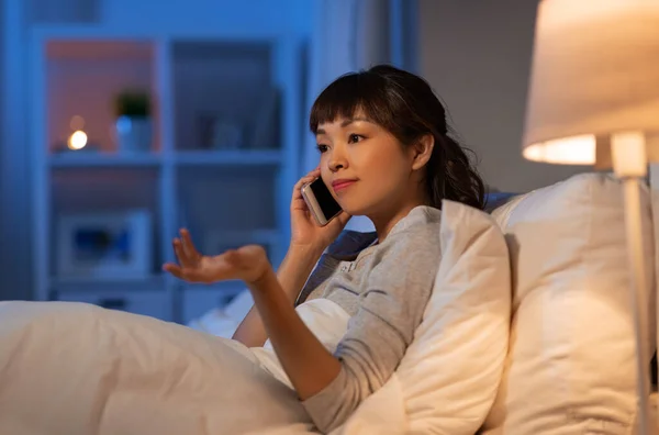 Asiática mulher chamando no smartphone na cama à noite — Fotografia de Stock