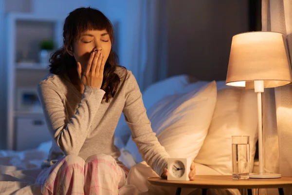 Mujer asiática con reloj bostezando en la cama por la noche —  Fotos de Stock
