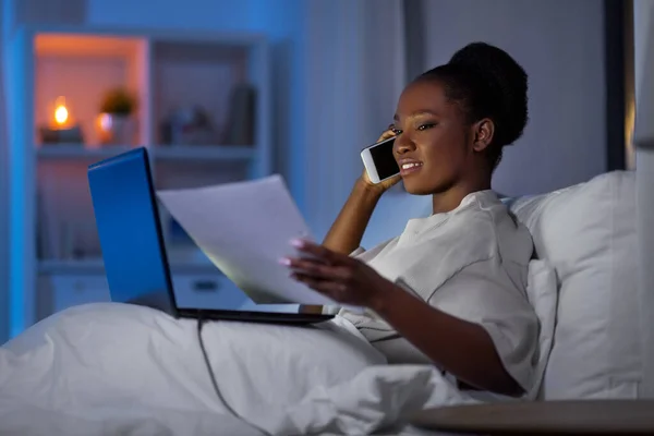 Mujer con portátil llamando en el teléfono inteligente en la cama —  Fotos de Stock