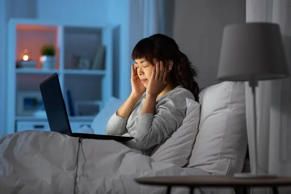 Напряженная женщина с ноутбуком работает в постели ночью — стоковое фото