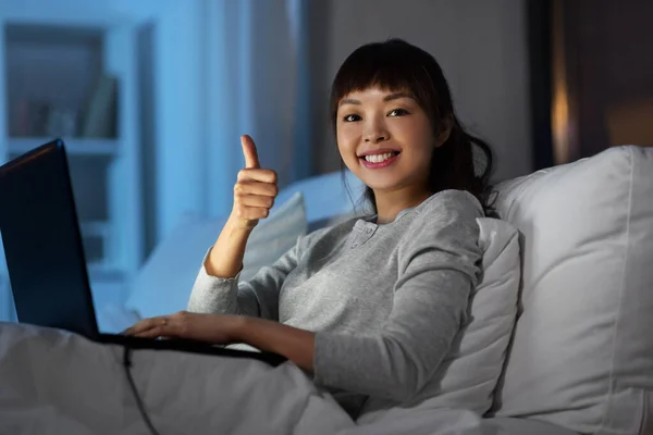 Vrouw met laptop in bed 's nachts shows duimen omhoog — Stockfoto