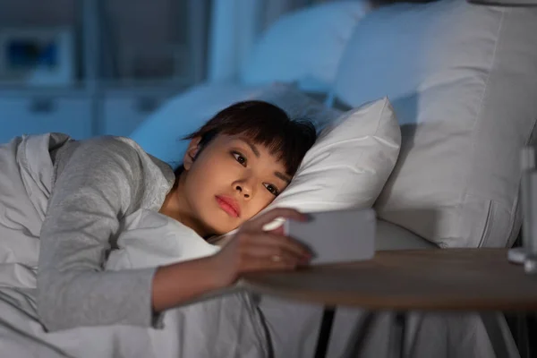 Aziatische vrouw met smartphone in bed 's nachts — Stockfoto