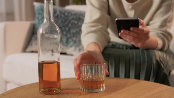 Жінка зі смартфоном п'є алкоголь вдома — стокове відео