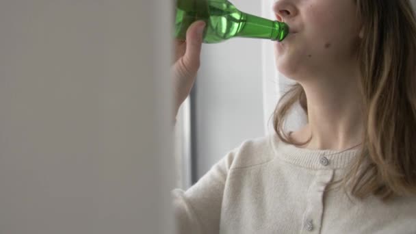 Женщина-алкоголик пьет пиво из бутылки дома — стоковое видео