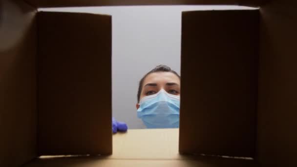 Женщина в маске открывает коробку с лекарствами — стоковое видео