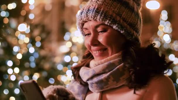 Mujer feliz con teléfono inteligente en la ciudad de Navidad — Vídeos de Stock