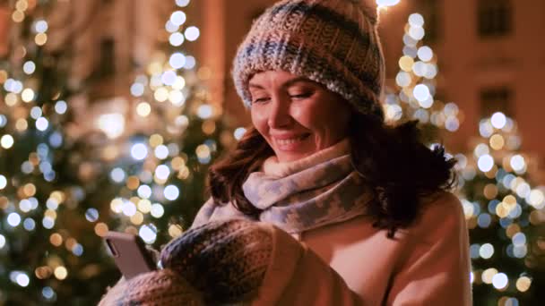 Щаслива жінка зі смартфоном у різдвяному місті — стокове відео