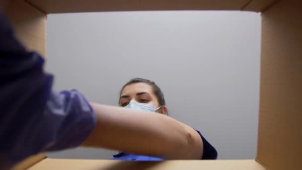 소포 상자에 옷을 채우고 있는 마스크를 쓴 여자 — 비디오