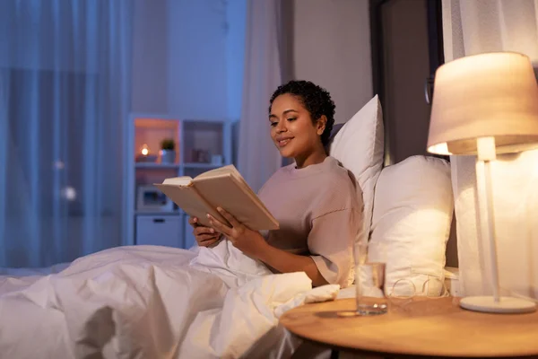 Улыбающаяся молодая женщина читает книгу в постели дома — стоковое фото