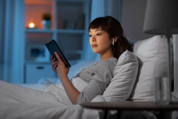Mujer con tablet pc en auriculares en la cama por la noche —  Fotos de Stock