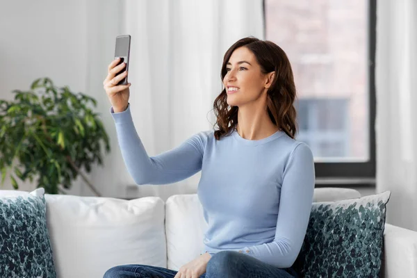 Mujer feliz con teléfono inteligente tomando selfie en casa —  Fotos de Stock