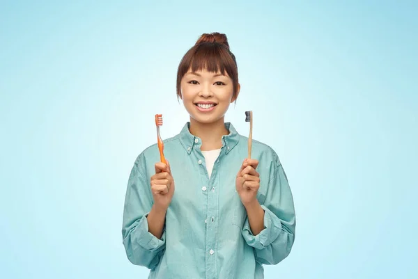 木製やプラスチック製の歯ブラシを持つアジアの女性 — ストック写真