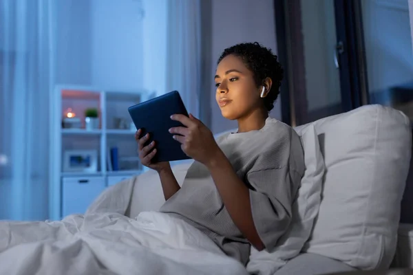 Wanita dengan tablet pc di earphone di tempat tidur di malam hari — Stok Foto