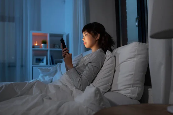 Mujer asiática con smartphone en la cama por la noche —  Fotos de Stock