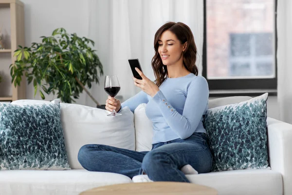 Nő okostelefonnal ivás vörösbor otthon — Stock Fotó