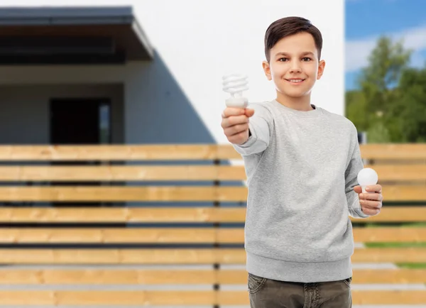 Boy comparing different light bulbs over house — Stock Photo, Image