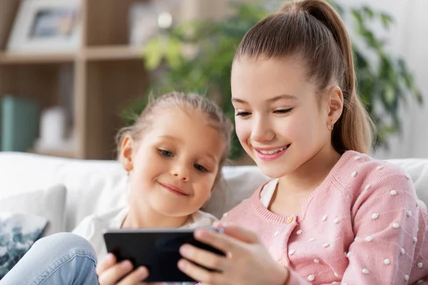 Niñas o hermanas felices con teléfono en casa —  Fotos de Stock