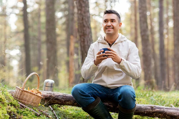 Man met mand champignons drinkt thee in het bos — Stockfoto