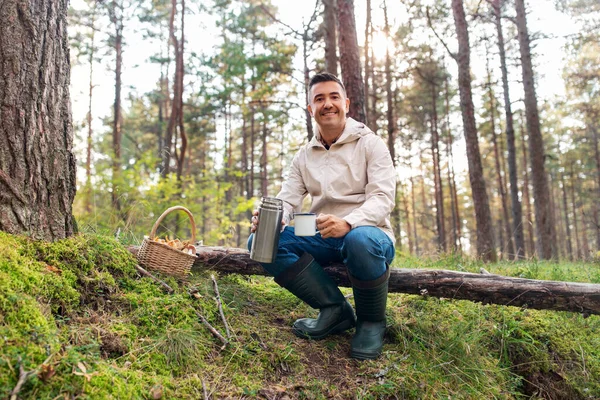 Человек с корзиной грибов пьет чай в лесу — стоковое фото