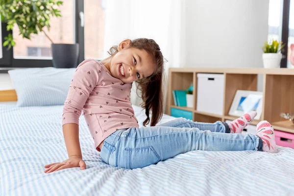 Gelukkig glimlachend klein meisje zitten op bed thuis — Stockfoto