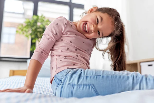 Happy smiling little girl sitting on bed at home — Stock Photo, Image