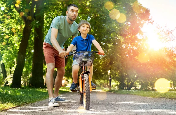 Padre enseñando a su hijo a montar en bicicleta en el parque — Foto de Stock