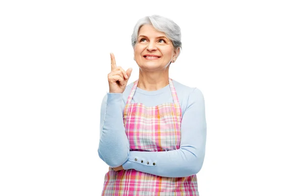 Tersenyum wanita senior di celemek menunjuk jari ke atas — Stok Foto