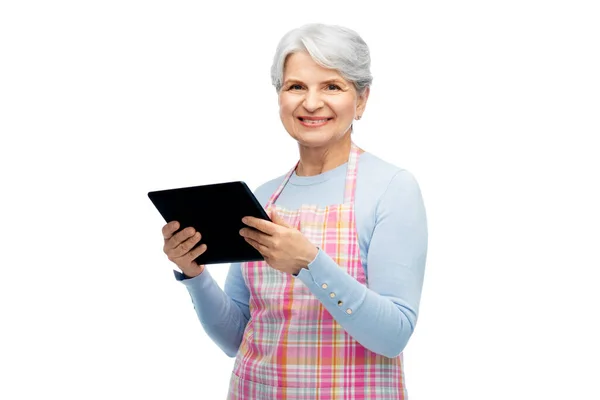 Усміхнена старша жінка в фартусі з планшетним комп'ютером — стокове фото