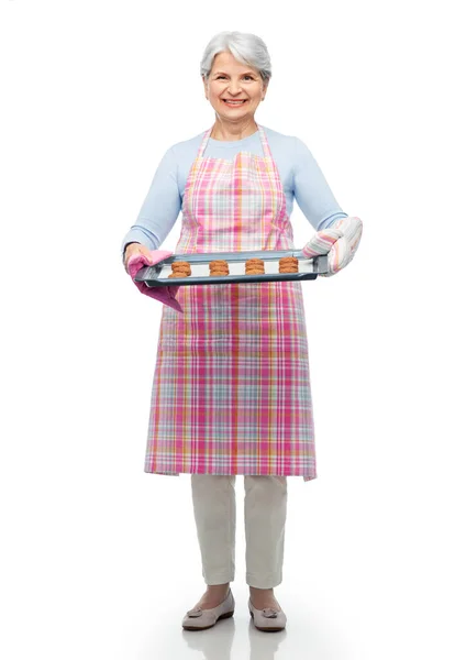 Senior vrouw in schort met koekjes op bakpan — Stockfoto