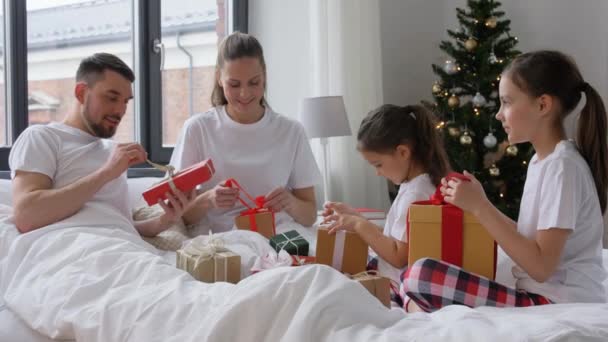 Счастливая семья с рождественскими подарками в постели дома — стоковое видео