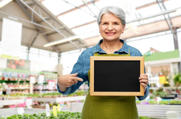 Happy senior woman with chalkboard at garden store — Stock Photo, Image