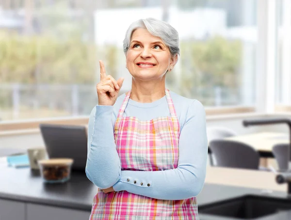 Mosolygó idős nő kötényben mutogatott ujjal felfelé — Stock Fotó