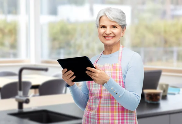 Щаслива старша жінка в фартусі з планшетним ПК вдома — стокове фото
