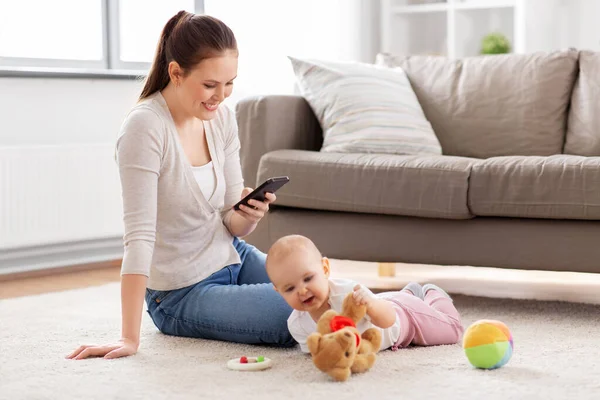 Mãe com smartphone e bebê brincando em casa — Fotografia de Stock