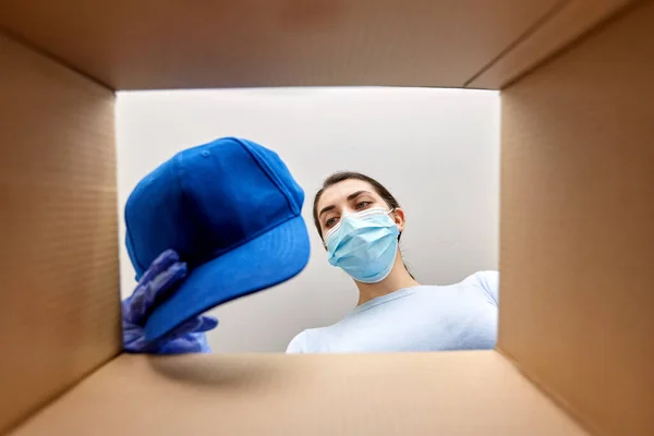 Vrouw in masker openen pakket doos met kleren — Stockfoto