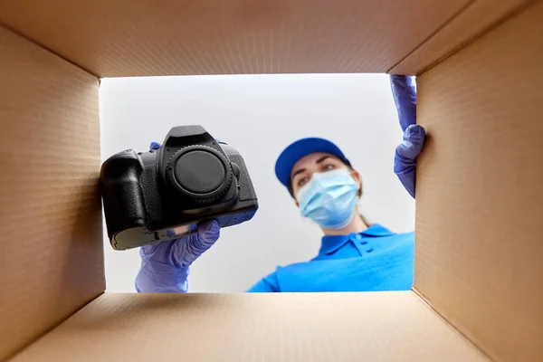 Kvinna i mask packning kamera i paket låda — Stockfoto