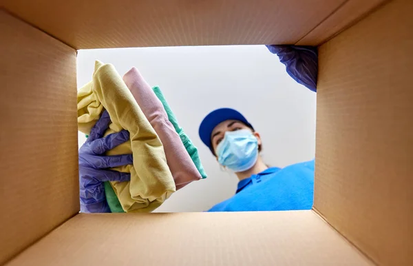 Kvinna i mask packning kläder till paket låda — Stockfoto